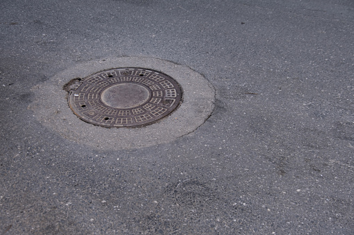 An old sewer manhole cover surrounded by an asphalt street