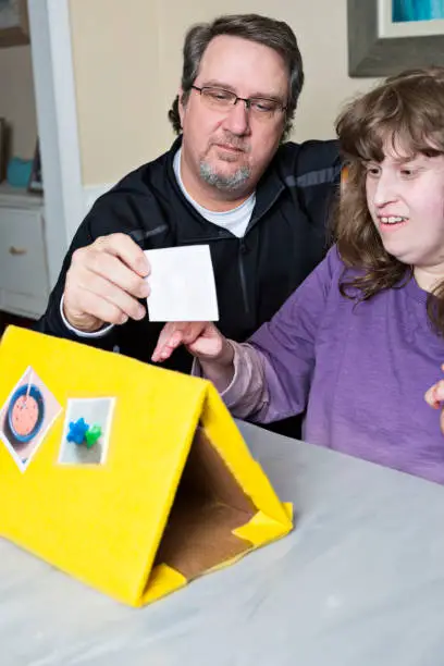 Dad of autistic and disabled female student holds up picture card for his nonverbal daughter while homeschooling during the pandemic