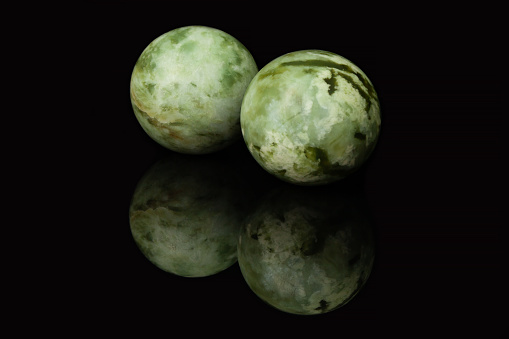 Two malachite balls, similar to two planets, lie on a glossy black glass, in which their reflection is visible