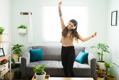 Playful young woman dancing alone at home and having fun. Beautiful woman listening to music with headphones during a relaxing day