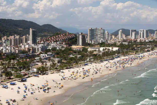Aerial view of Enseada Beach at Guaruja SP Brazil. People on the beach, the sand, sea waves and the city on background. Place known as Praia da Enseada. Brazilian coastal city.