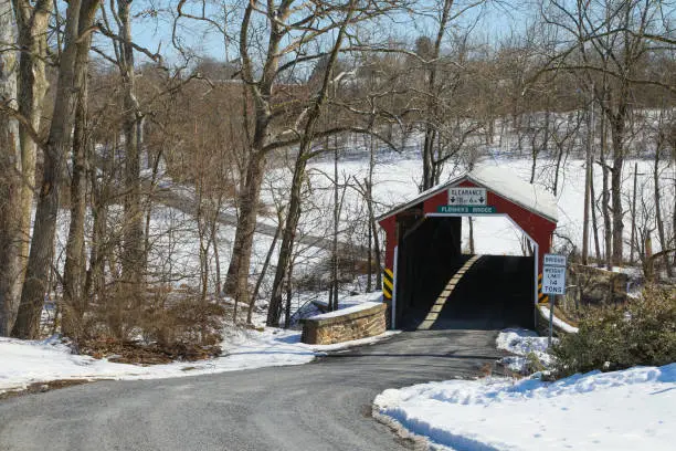 Wide angle winter scene of the Fleisher's covered bridge and a winding road,  in Perry County, PA, surrounded by snow and trees.