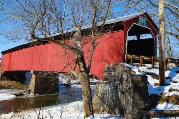 Horizontal image of the Fleisher's covered bridge, in Perry County, PA, with a stream, snow and trees.