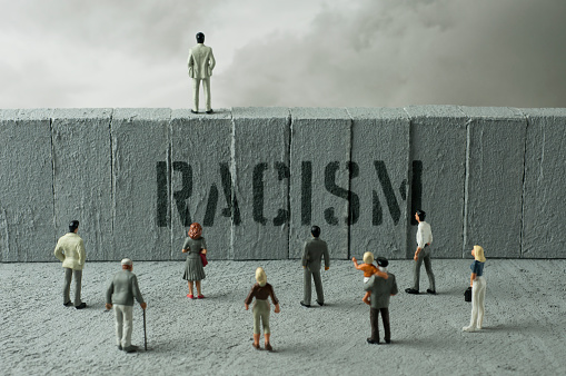 People figurines looking at the Racism warning on the wall. Uncertainty concept