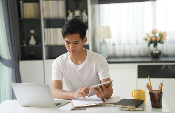 istock asian young student man entrepreneur working with tablet studying learning online at home. e-learning webinar meeting. social distance in covid pandemic 1304125788