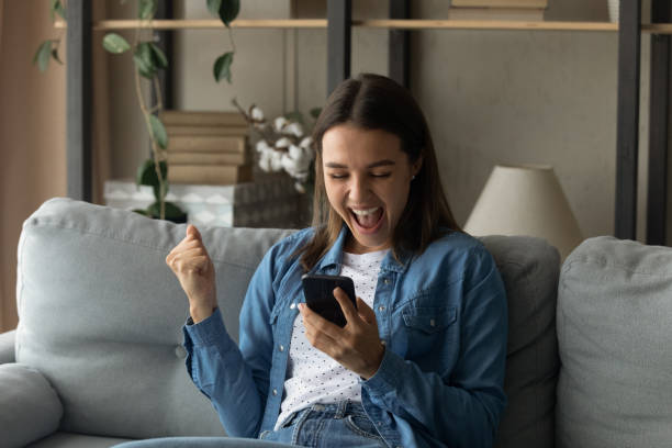 Amazed millennial female hold smartphone reading perfect job offer Amazed millennial female student hold smartphone yell in delight motivated with new opportunities reading perfect job offer. Happy young woman feel lucky celebrate receiving unexpected lottery prize super money stock pictures, royalty-free photos & images
