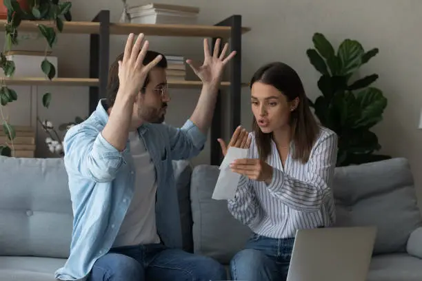 Stressed emotional couple arguing fighting when checking financial papers together finding unexpected debt lack of money on bank account. Mad angry husband scolding wife for overspending family budget