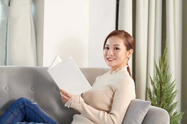 istock Pretty young woman relaxing reading a book on a comfortable sofa at home 1304133985
