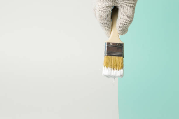 istock A gloved hand holds a paint brush with white paint on a two-tone background. 1304136122