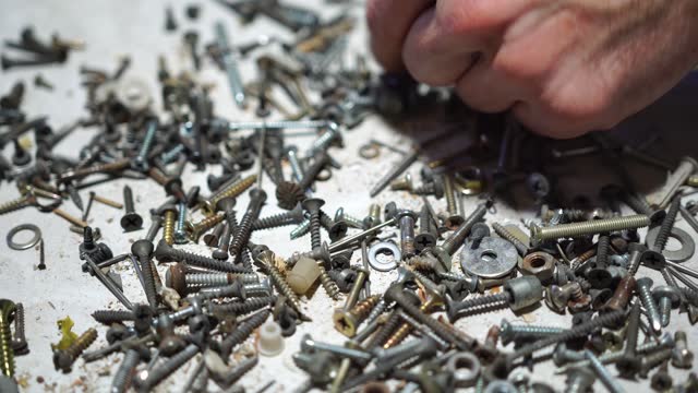 hand putting and sorting screws, nails, bolts and washers on the table. Selective focus, close up