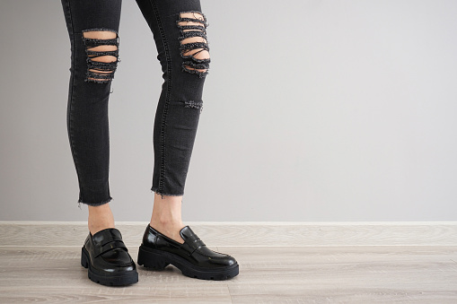Legs of a young girl in black jeans and black shoes on a gray background, space for text.
