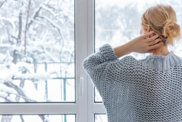 una donna guarda fuori dalla finestra all'aperto innevato - snow heat adult blond hair foto e immagini stock