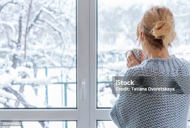 A Woman Looks Out Of The Window At The Snowcovered Outdoors Stock Photo - Download Image Now