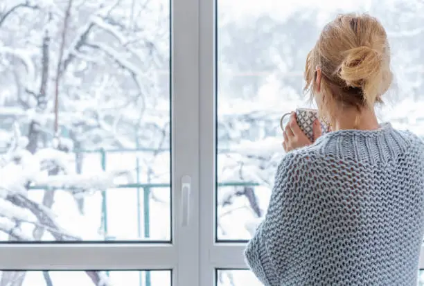 Photo of A woman looks out of the window at the snow-covered outdoors