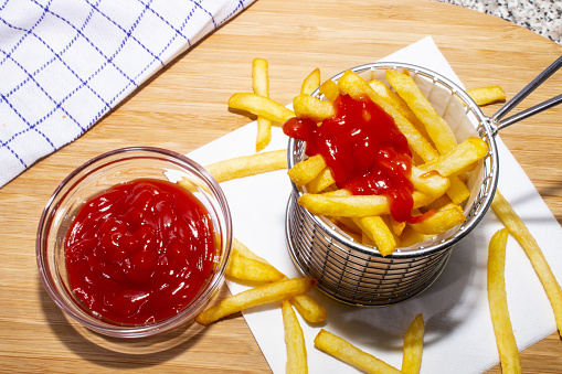 french fries in a metal basket and tomato ketchup in a glass bowl