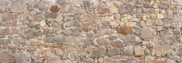 Panorama - Old gray brown wall made of many different natural stones in irregular arrangement