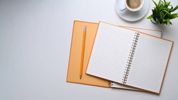 istock Overhead view of empty notebook, coffee cup, house plant and copy space on white table. 1304153980