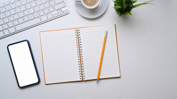 istock Modern white office desk with smart phone, notebook, keyboard, coffee cup and notebook on white background. 1304154553