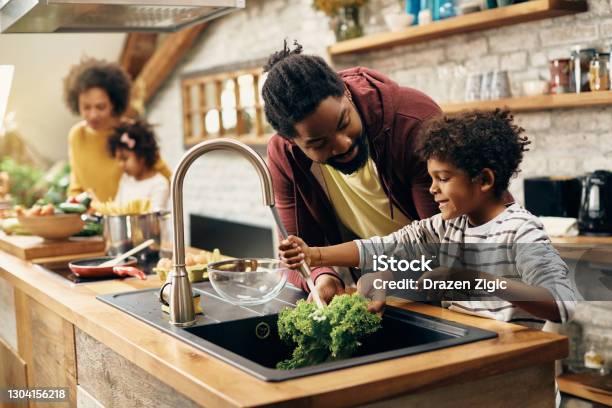 Happy Black Father And Son Cleaning Vegetables While Preparing Food In The Kitchen Stock Photo - Download Image Now