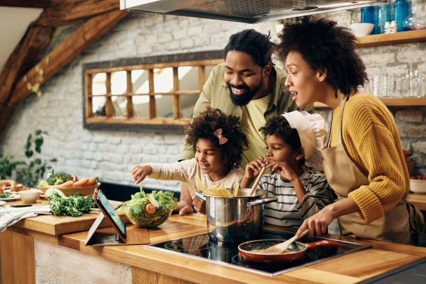 feliz familia negra siguiendo la receta en el panel táctil mientras cocina en la cocina. - espagueti fotos fotografías e imágenes de stock