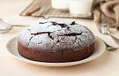 Chocolate sponge flourless cake with sugar powder, light concrete background. Brownie cake. Toned image.