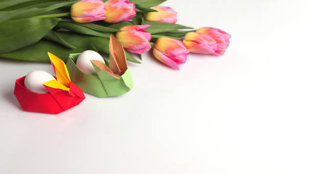 istock Easter still life on an isolated background. Paper rabbits. Origami. Easter eggs. On a white table-a bouquet of tulips. Copy space 1304158410