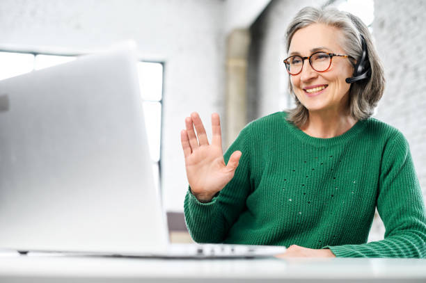 istock Cheerful aged woman with headset greeting by video 1304164695