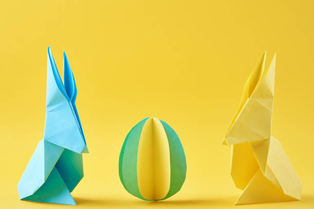 istock Two paper origami Esater rabbits and colored egg on yellow background. Easter celebration concept 1304167015