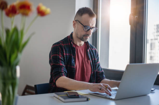 istock Handsome middle-aged man in glasses working home looking into laptop screen 1304169331