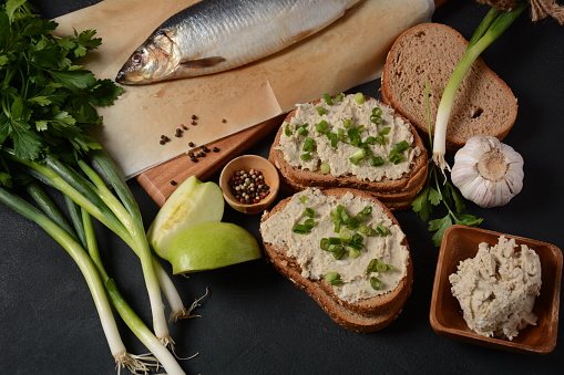 Traditional Jewish snack vorschmack or forshmak with bread and green onion, made of herring fillet and served with rye bread, dark stone background