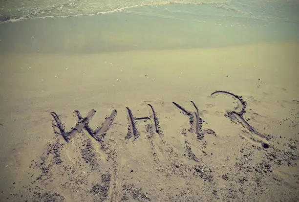 Big text WHY written in the sand of the beach by the sea with question mark