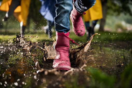 Close up of unrecognizable kid having fun while running through muddy puddle in the park.
