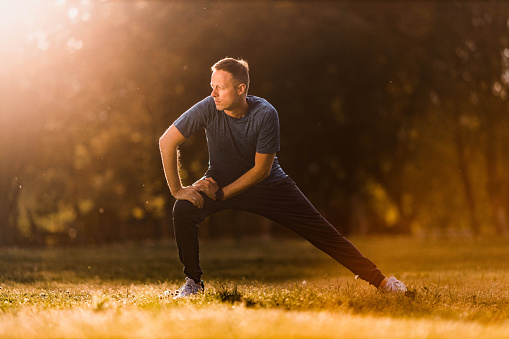 Young athletic man doing stretching exercises in nature. Copy space.