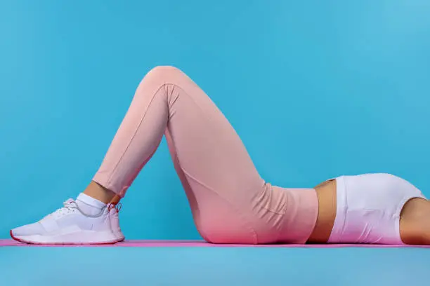 Photo of Woman doing exercises with resistance bands at home. Cropped shot of a young fit woman exercising on the floor. Workout at home, quarantine, body care concept on blue background