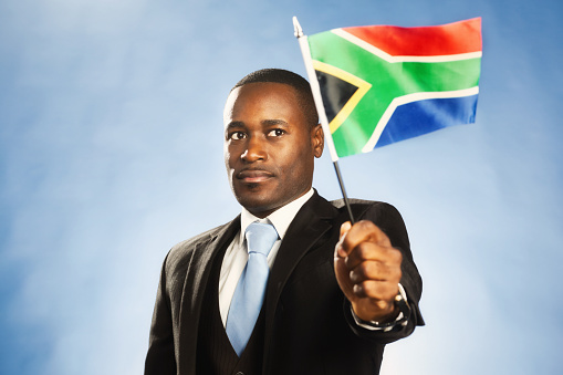 Formally dressed man in a three-piece suit holds a minature version of the South African flag.