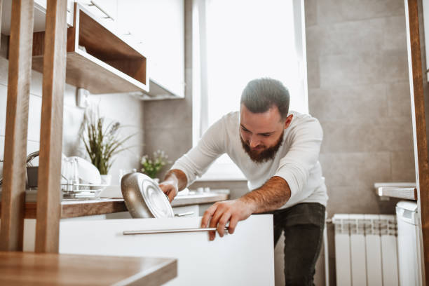 Male Sorting Out Pans And Plates After Washing Them In Kitchen