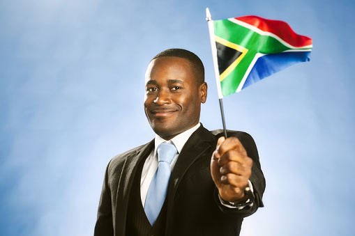 Formally dressed man in a three-piece suit holds a minature version of the South African flag.