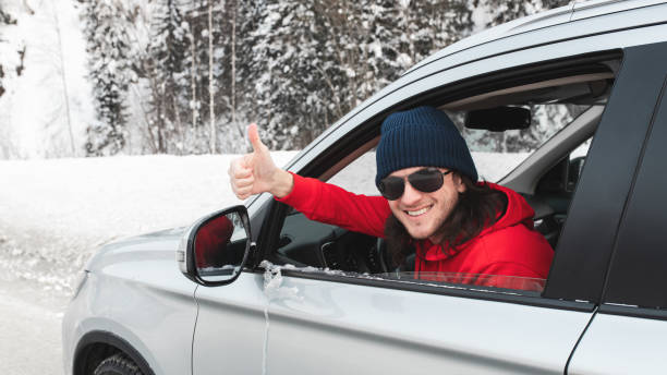 행복한 미소 긴 머리 남자는 차에 앉아 얼음 도로에 화창한 겨울 날에 열린 측면 창을 통해 엄지 손가락을 표시. - ski insurance 뉴스 사진 이미지