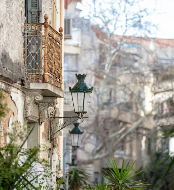 Old lantern on a ruined building wall, rusty iron balcony, peeled stonewall background. Aged abandoned antique buildings, architecture in Greece.