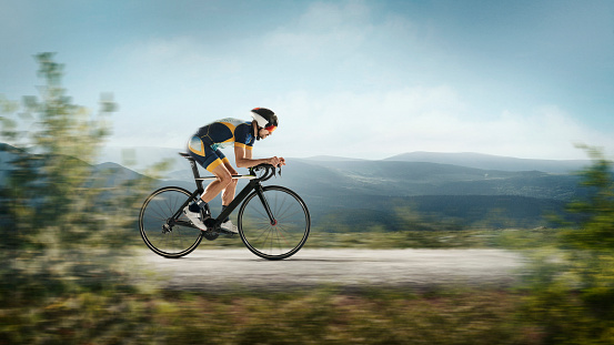 On the run. Triathlon male athlete cycle training on mountains background. Caucasian fit triathlete practicing in cycling wearing sports equipment. Concept of healthy lifestyle, sport, action, motion.