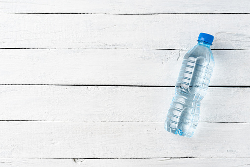 Overhead shot of mineral water in small plastic bottle on white wooden background with copyspace