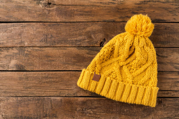 istock Yellow winter hat with pompon on wooden background with copyspace. Top view 1304181437