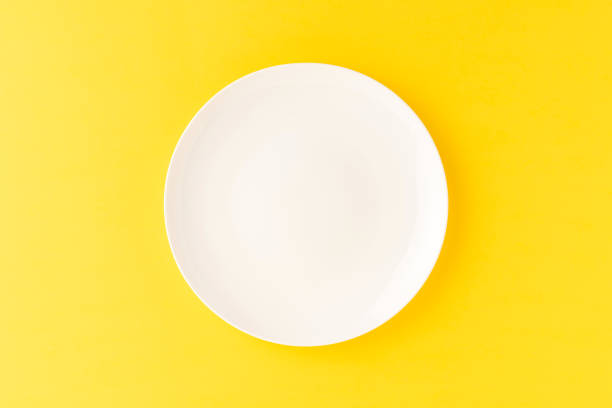 istock Overhead shot of empty white plate on yellow table. Close up 1304181615