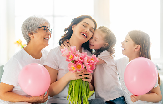 Happy women's day! Child daughters are congratulating mom and granny giving them flowers tulips. Grandma, mum and girls smiling and hugging. Family holiday and togetherness.