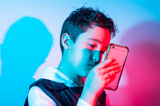 istock Child looking at cell phone under red and blue neon lights. Horizontal studio shot. 1304186840