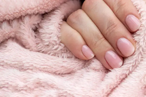 Female hands with beautiful manicure - pink nude nails on pale pink fluffy fabric, textile background, closeup with copy space.