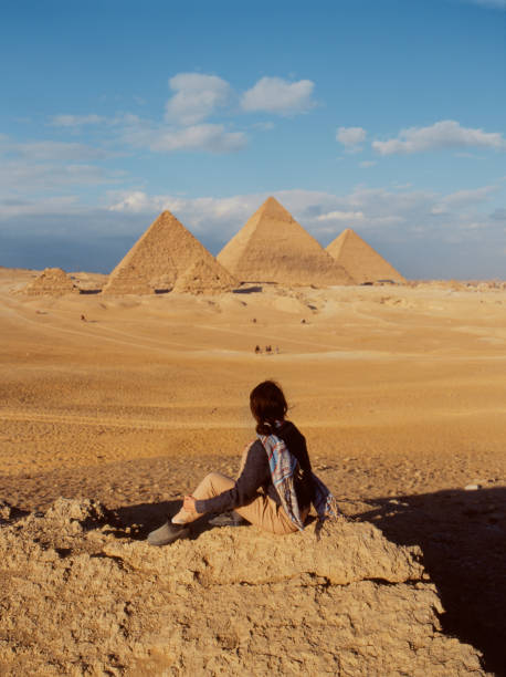 femme s’asseyant dans le désert près des pyramides de gizeh - tourist egypt pyramid pyramid shape photos et images de collection