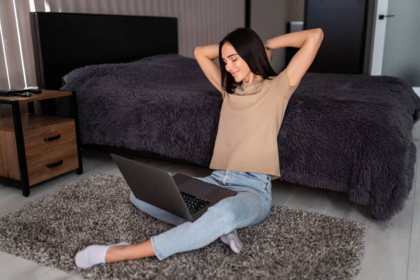 インターネット上で働く彼女のリビングルームでリラックスしたコンピュータで床に座って現代の家で若い健康な女性。 - yoga business women living room ストックフォトと画像