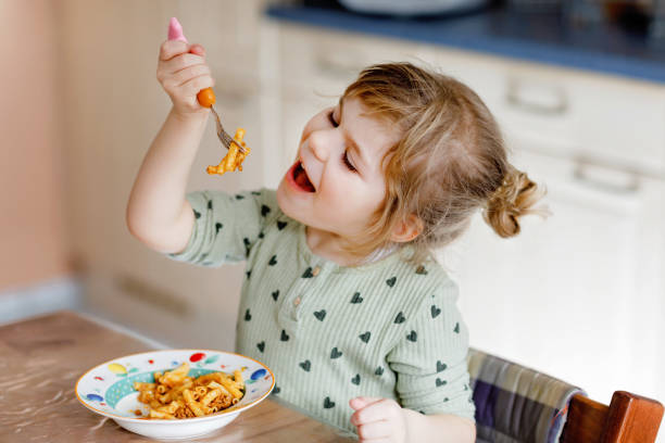 愛らしい幼児の女の子は、ミンチ肉とパスタマカロニボロネーゼを食べます。屋内、自宅で麺や野菜と新鮮な調理された健康的な食事を食べる幸せな子供。 - child eating pasta spaghetti ストックフォトと画像