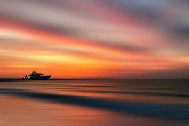 Photo of Colorful sunset with yacht at the horizon line at beautiful Gulf sea, motion blur effect with clods and wave. Vacation time to relax and enjoy life.